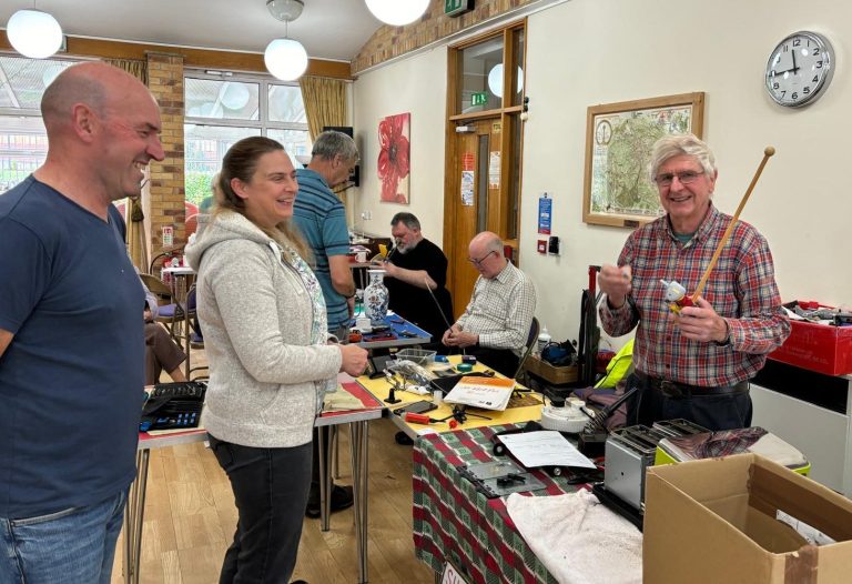 A small community event with people socialising and selling various items at tables.