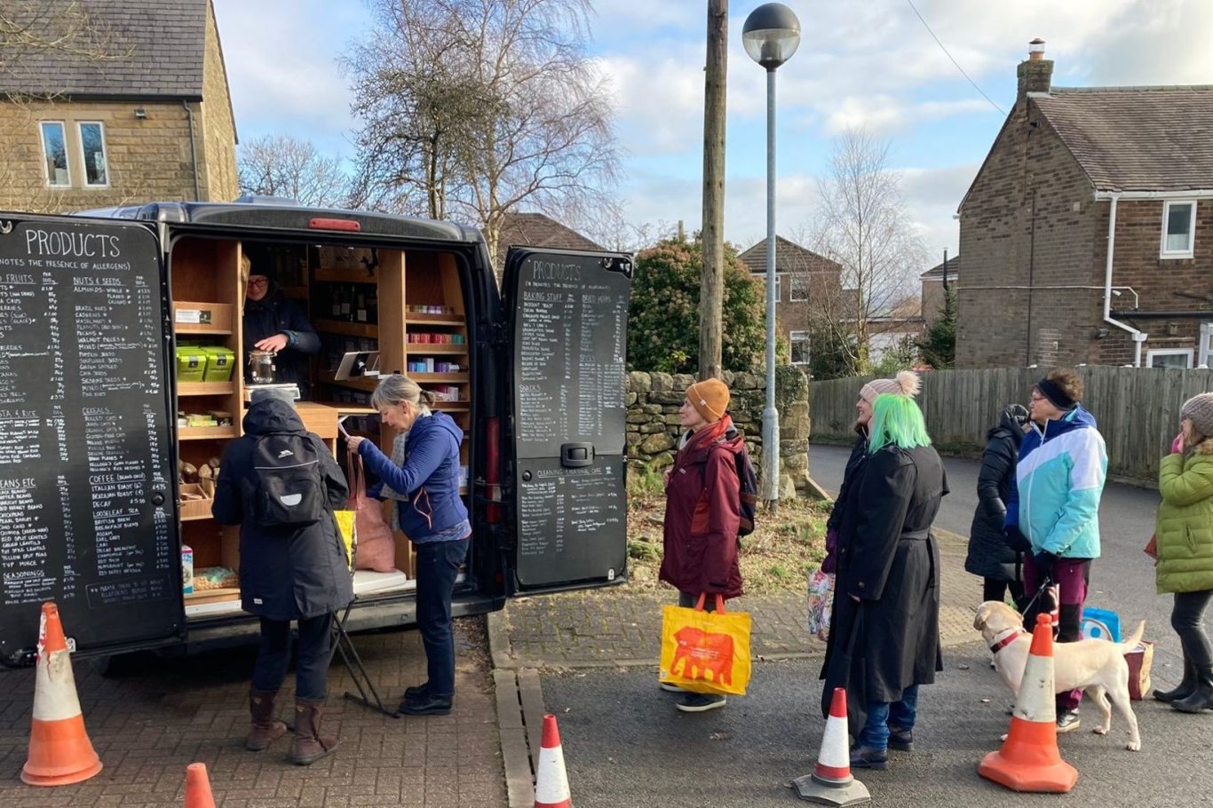 A van providing refills of food and household items, with customers lined up, near residential houses.